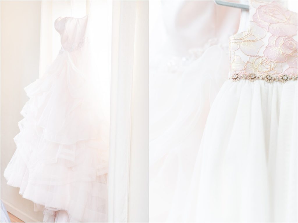 bride's dress hanging in front of window with flower girl's dress