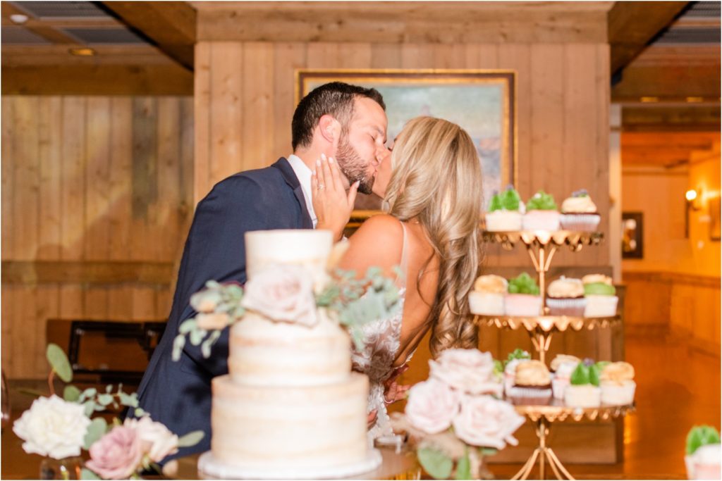 wedding couple kissing behind wedding cake in rustic barn