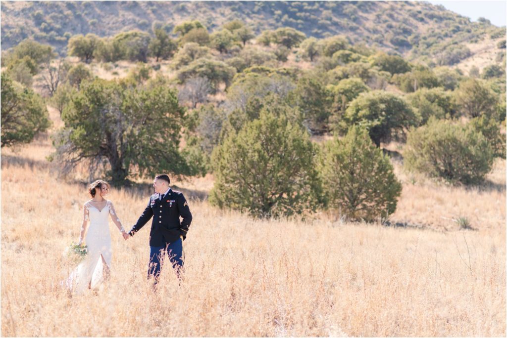couple smiling and walking through an open field together