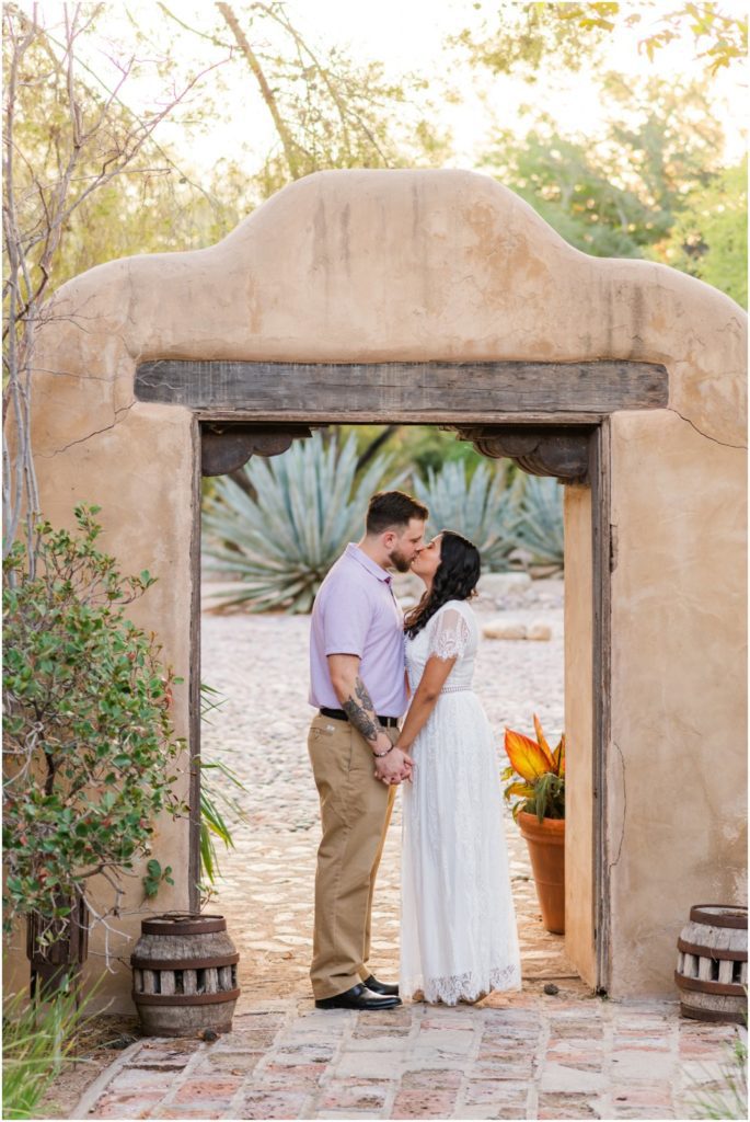 engaged couple in Tucson kissing under adobe archway during engagement sessin