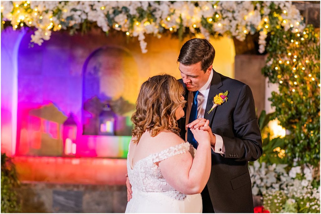 bride and groom dancing with rainbow lighting behind them