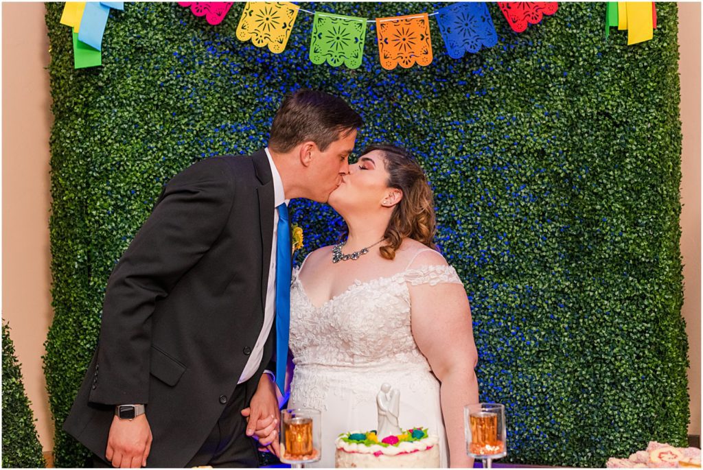 bride and groom kiss behind wedding cake