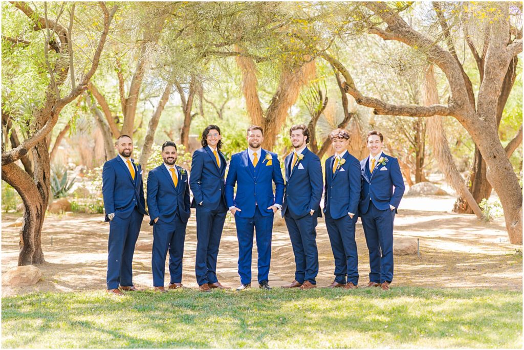 groom and groomsmen standing in grass in navy suits with gold ties