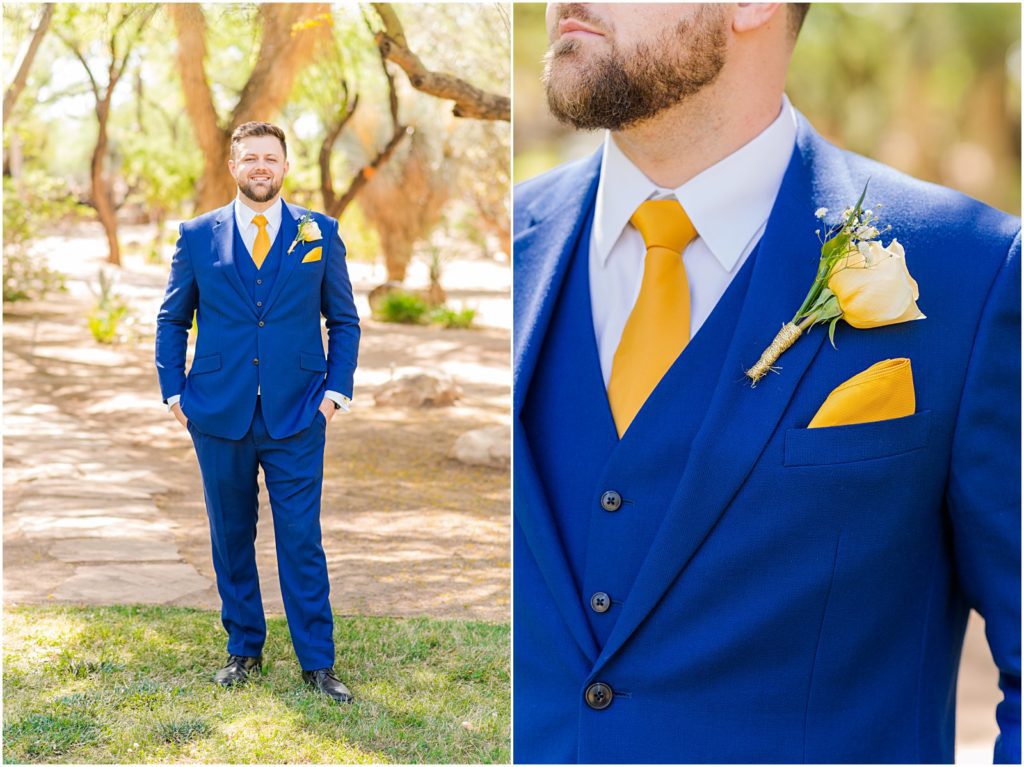 groom in navy suit with gold tie standing in grass with his hands in his pockets
