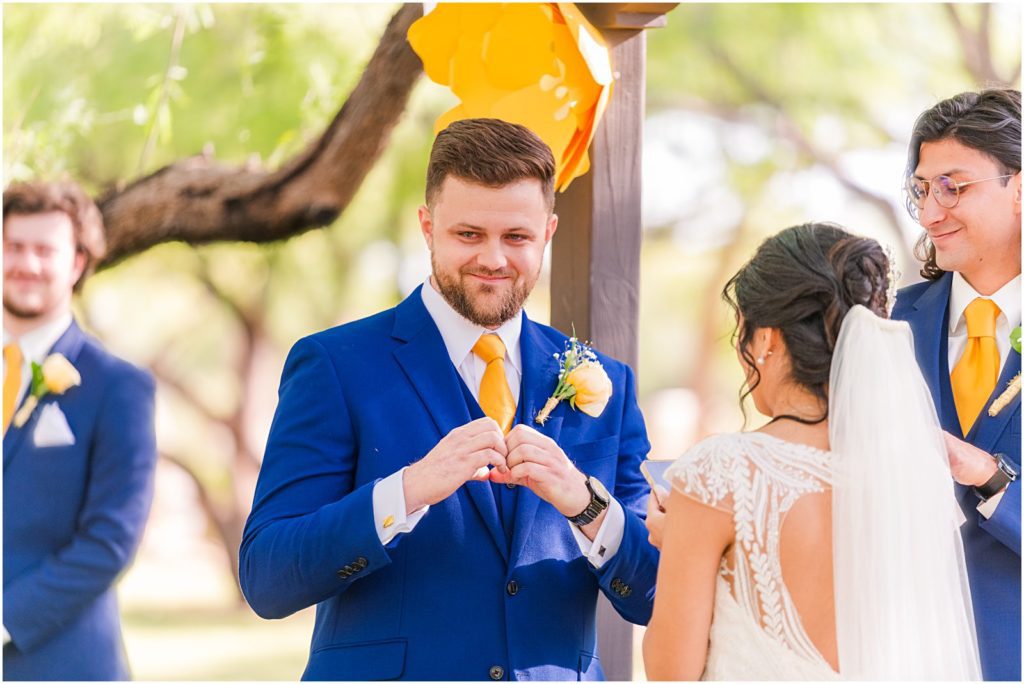 groom smiling and making a heart shape with his hands at in-laws during ceremony