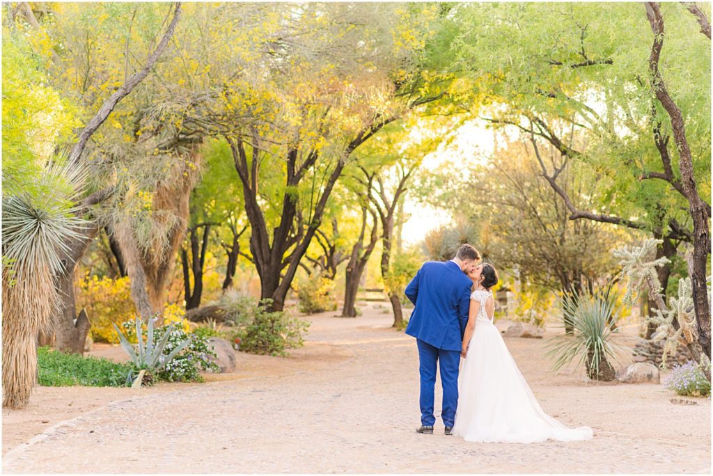 bride and groom kiss under mesquite trees with their backs to the camera