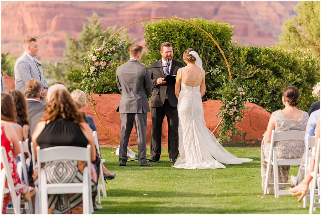 bride and groom standing at floral arch during Sedona wedding ceremony