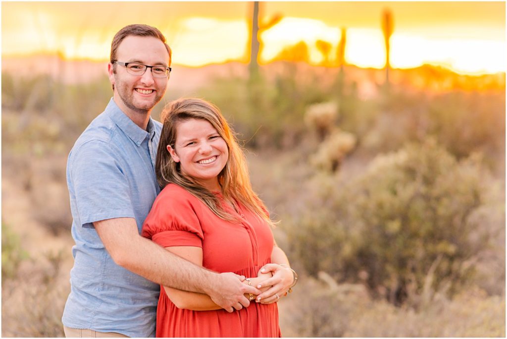 couple smiling at camera with desert sunset behind them
