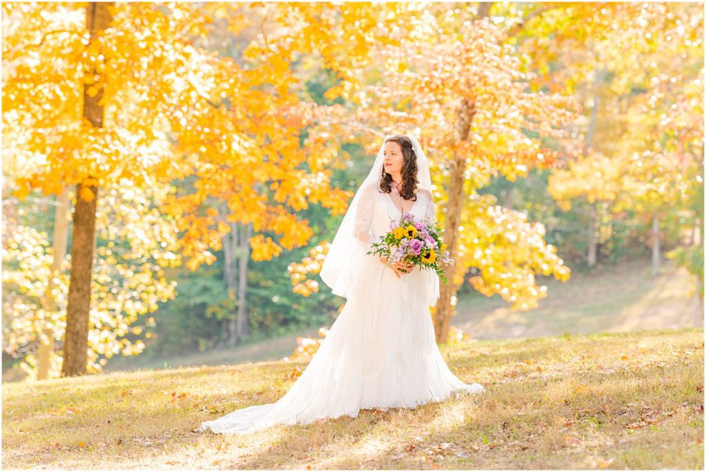 bride standing in woods around fall leaves