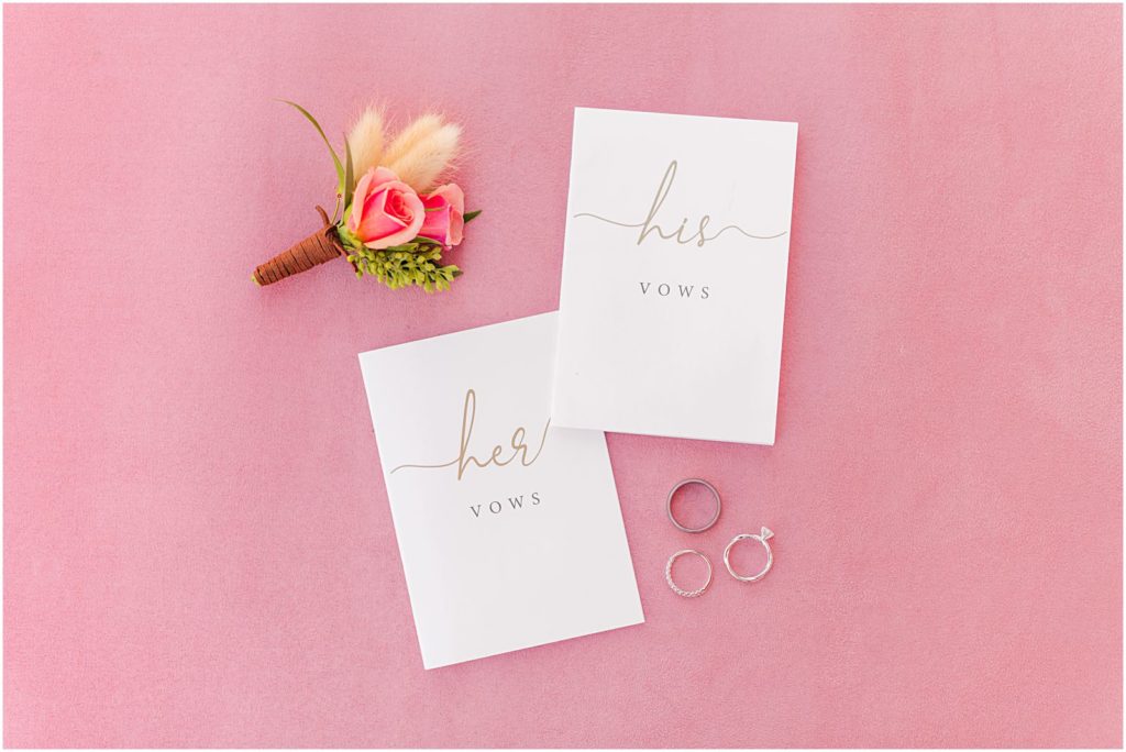 customized vow books on pink background with wedding rings and flowers