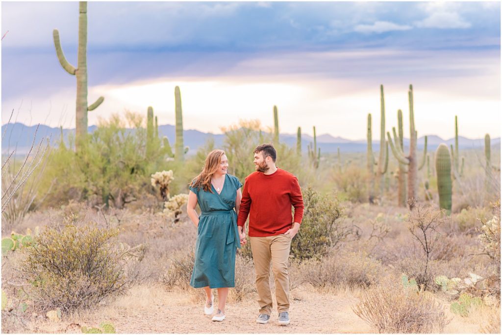 engaged couple walking together holding hands during windy desert engagement session in Tucson