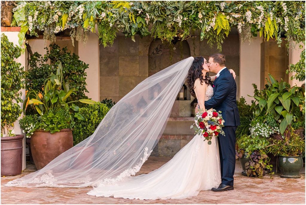romantic bride and groom kissing underneath arbor with long flowing veil