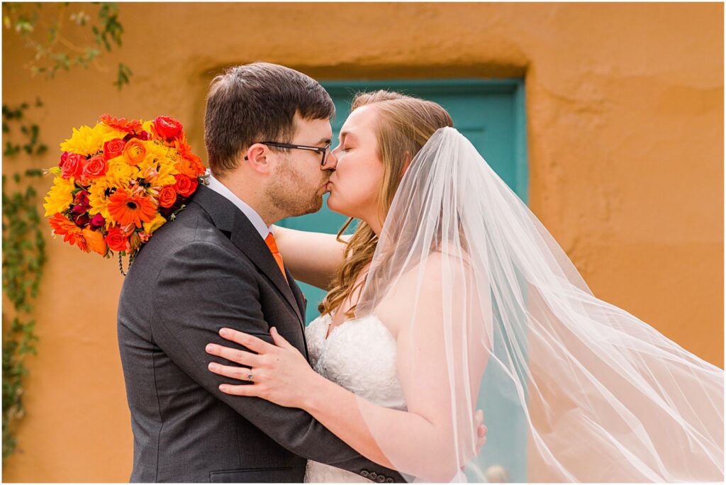 bride and groom kiss while veil blows in wind