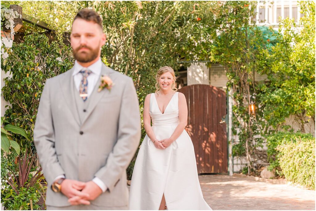 bride standing behind groom smiling before he turns around