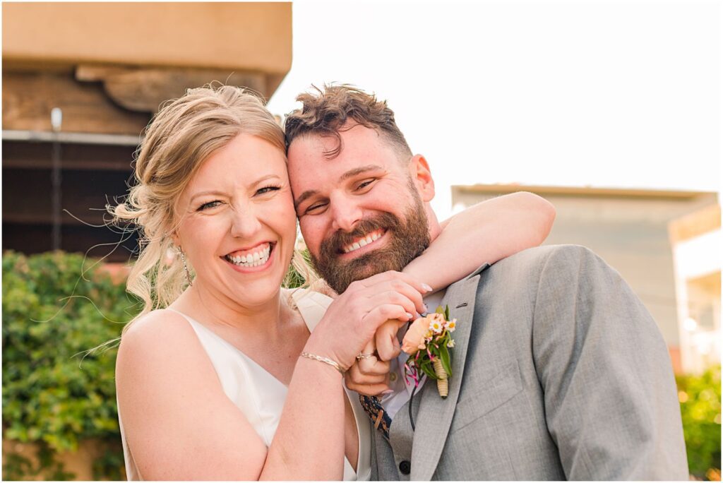 bride with arm around groom's neck as they both smile big at camera