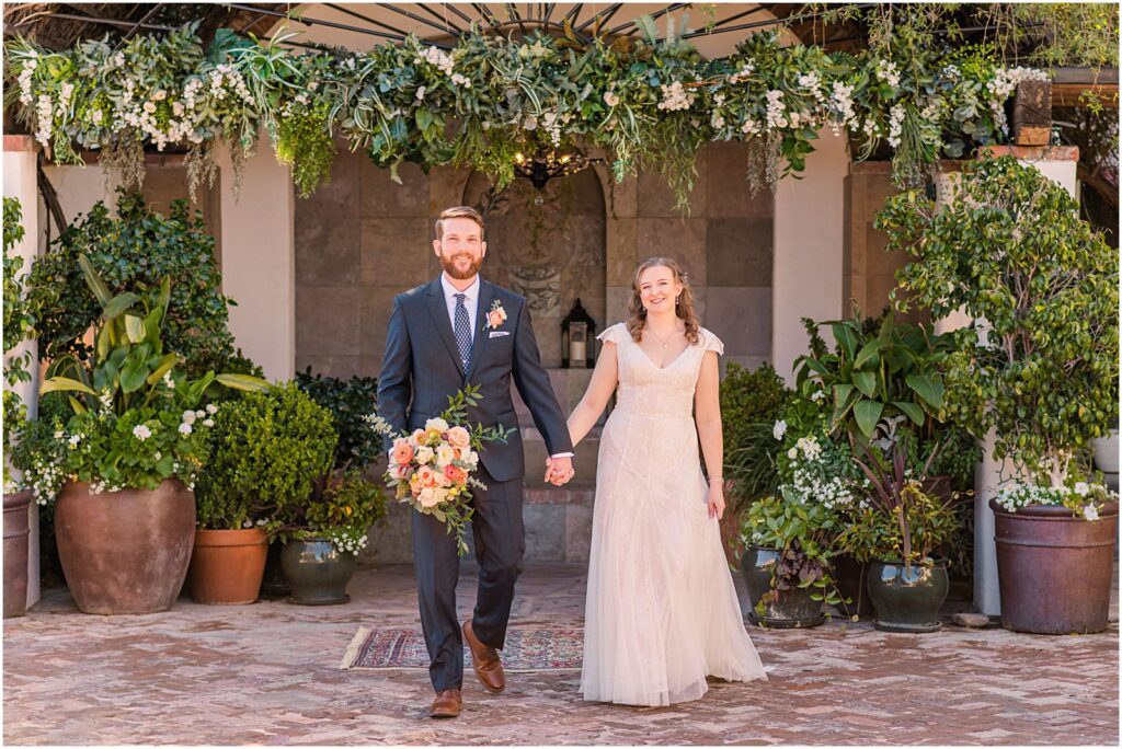 bride and groom walking and holding hands in garden courtyard