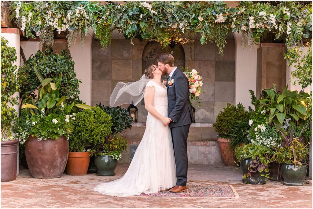 bride and groom kiss under arbor in garden courtyard