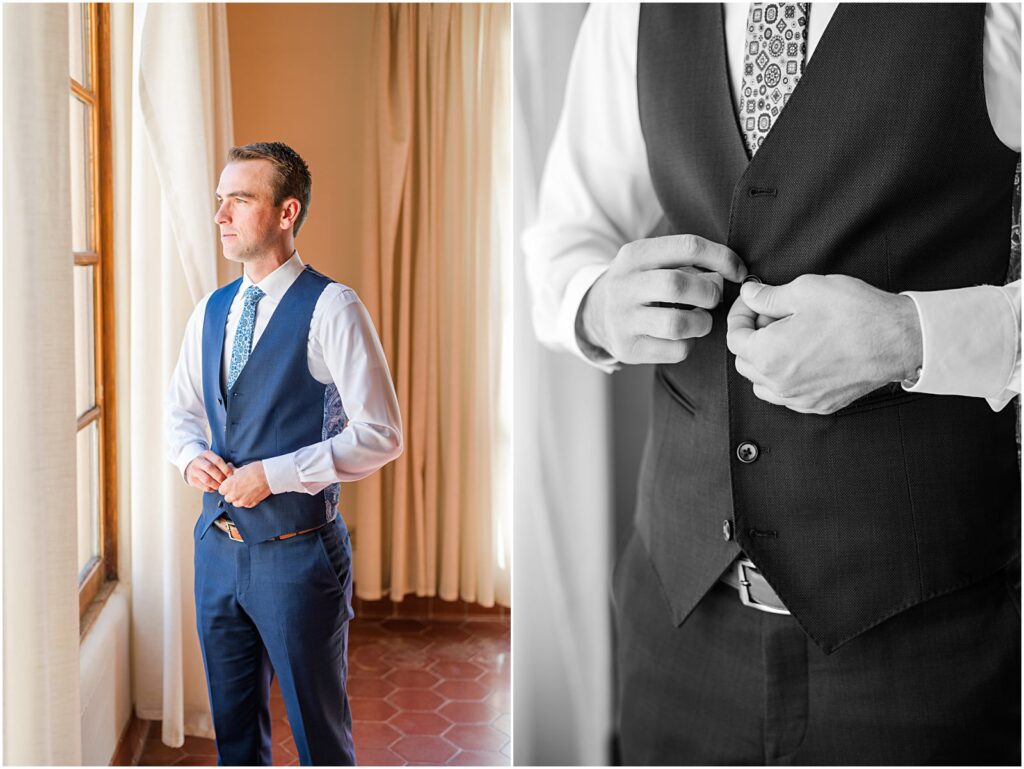 groom buttoning up his vest in front of window